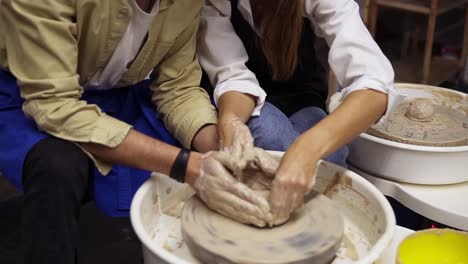 dirty couple's hands close up . romantic couple in love working together on potter wheel and sculpting clay pot. woman pouring water, working together in craft studio workshop. no faces