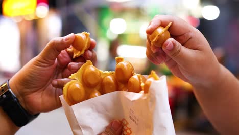 hands sharing bubble waffles on a busy street