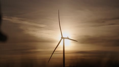 a wind turbine spins against a dramatic sunset as people walk by in slow motion