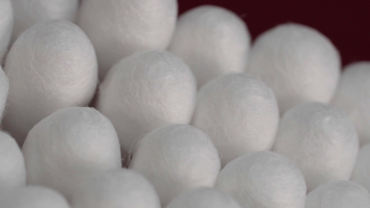 Primo piano in panoramica a sinistra di cotton fioc raggruppati con morbide punte di cotone bianco, che creano un motivo pulito e ripetuto su uno sfondo rosso. Prodotto per l'igiene quotidiana e la cura personale.