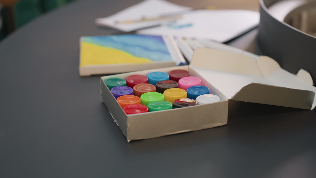 Preparación artística creativa, paleta de colores y lienzo preparados, botes de pintura intensos colocados cerca de un pequeño lienzo pintado, pulcro estudio artístico con colores vivos y pequeñas obras de arte pintadas