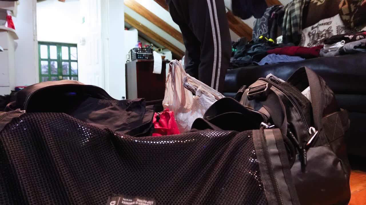 Man Folding and Packing Clothes into Black Suitcase at Home