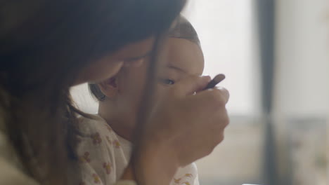 close up of a mom sitting at kitchen table and feeding her baby daughter with apple puree