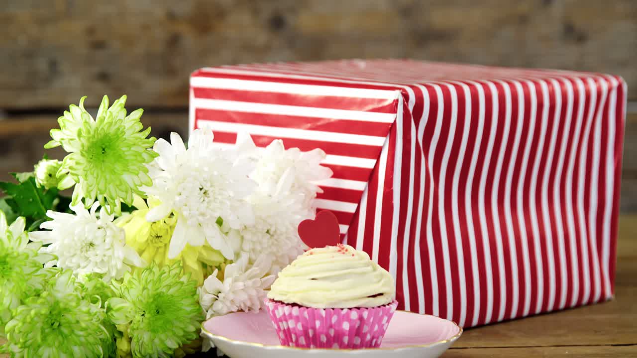 선물 상자, 꽃, 나무판 위에 있는 접시에 있는 컵케이크