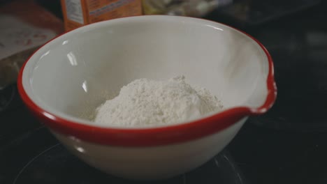 pouring a cup of white flour into a bowl - close up