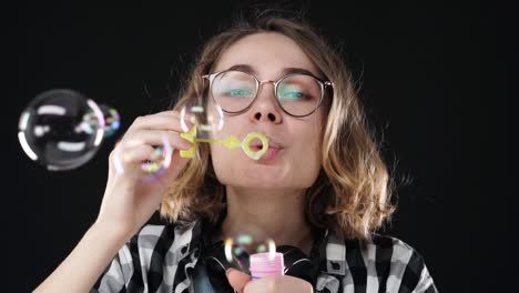 retrato en primer plano de una chica feliz y emocional soplando muchas burbujas de jabón con un palo en fondo negro. imágenes de estudio de una morena con cabello corto y labios sensuales con auriculares en el cuello. cámara lenta