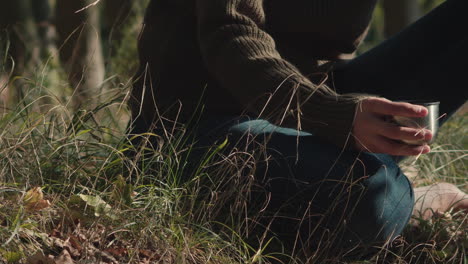 Close-up-of-a-person-sitting-in-nature-holding-a-cup-from-a-thermos-with-a-hot-drink