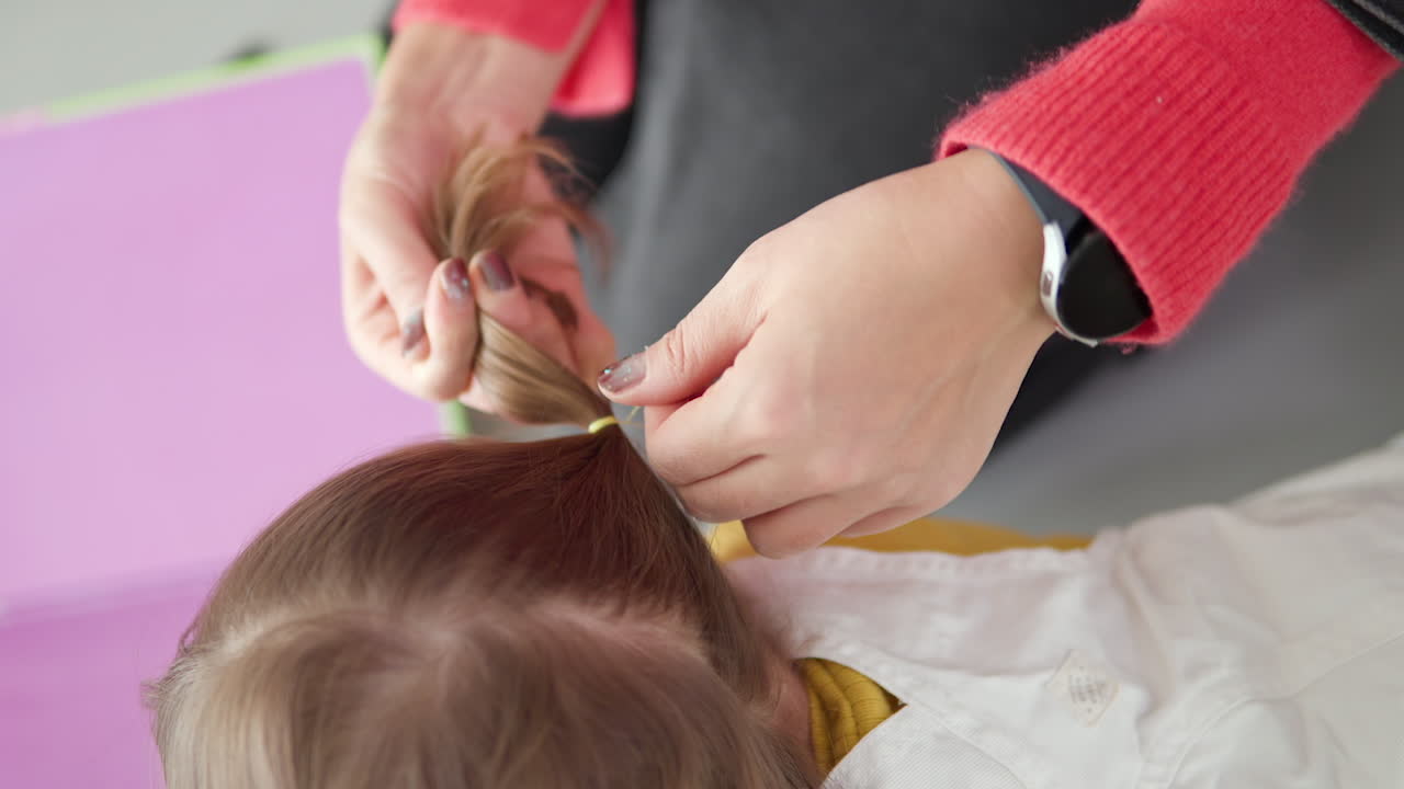 Mani della madre che legano i capelli della figlia usando elastici per capelli a casa - al rallentatore.