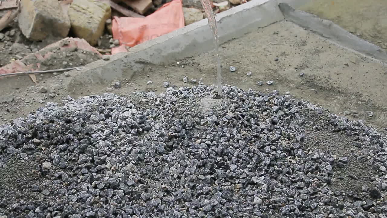 Indian mason worker pouring water over gravel to mix for construction or landscaping project