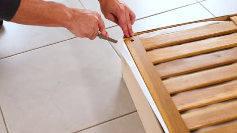 hands carefully cut open a wooden slatted box on a tiled floor using a knife, highlighting precision and focus