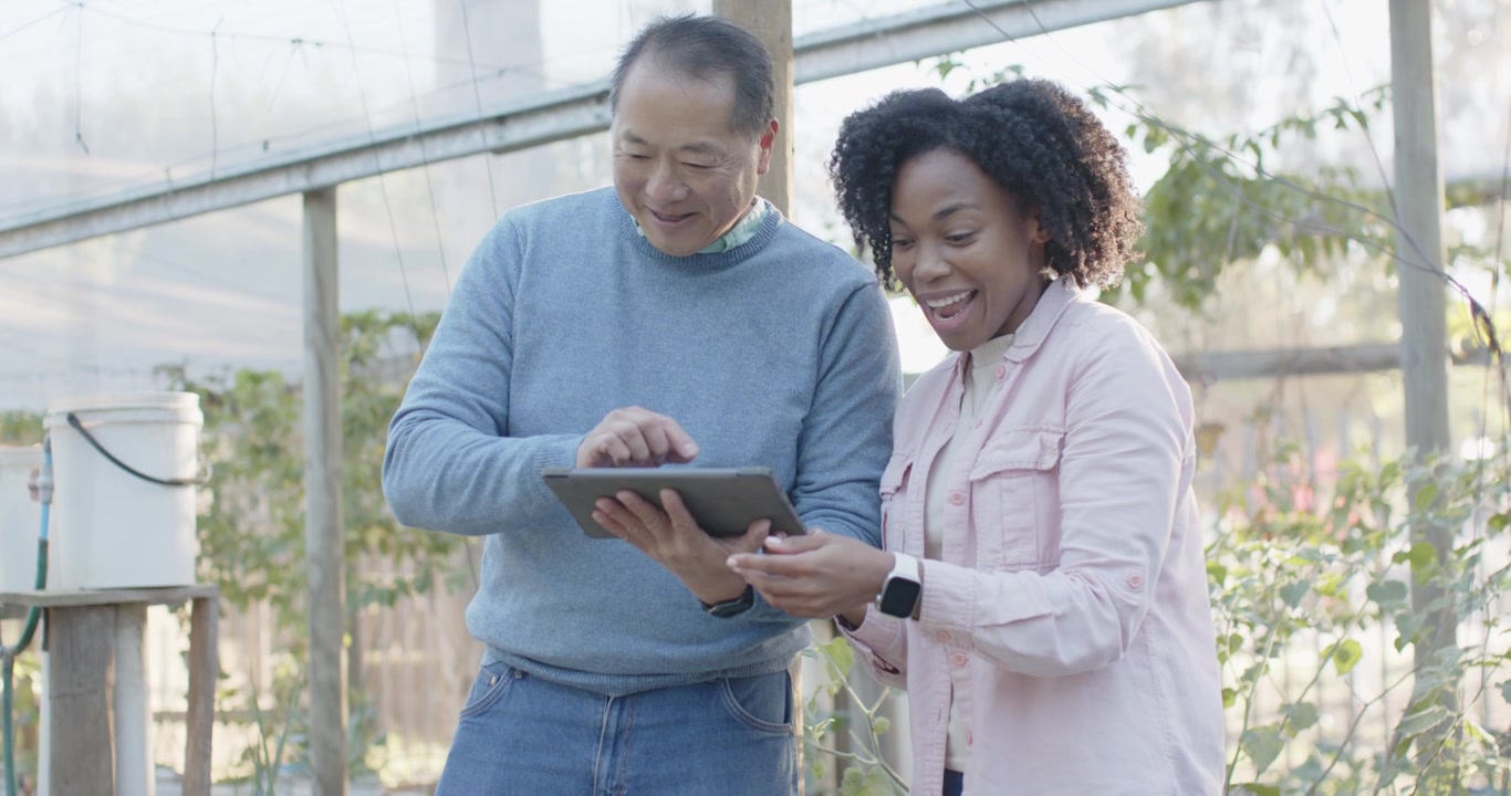 Diverse coworkers woman pointing at tablet, man tapping it in greenhouse while checking plant data