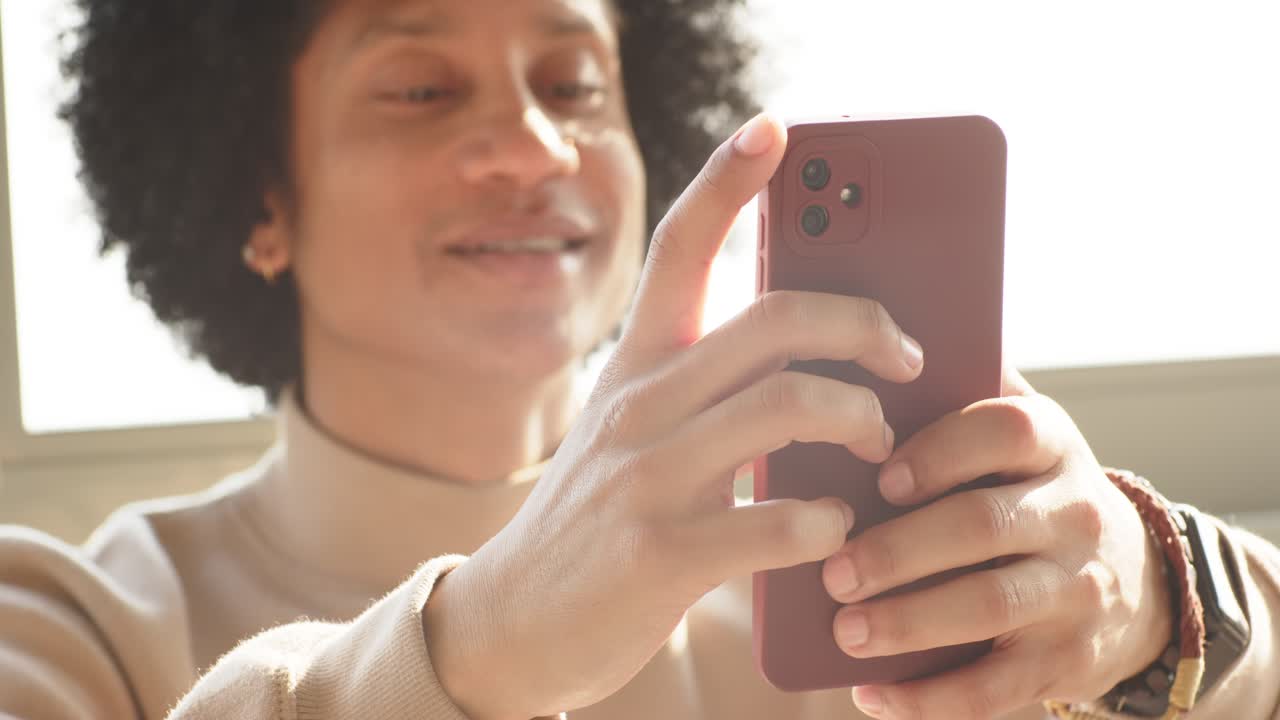 Uomo afroamericano di mezza età che prende uno smartphone rosso e modifica l'angolo di inquadratura del viso vicino alla finestra