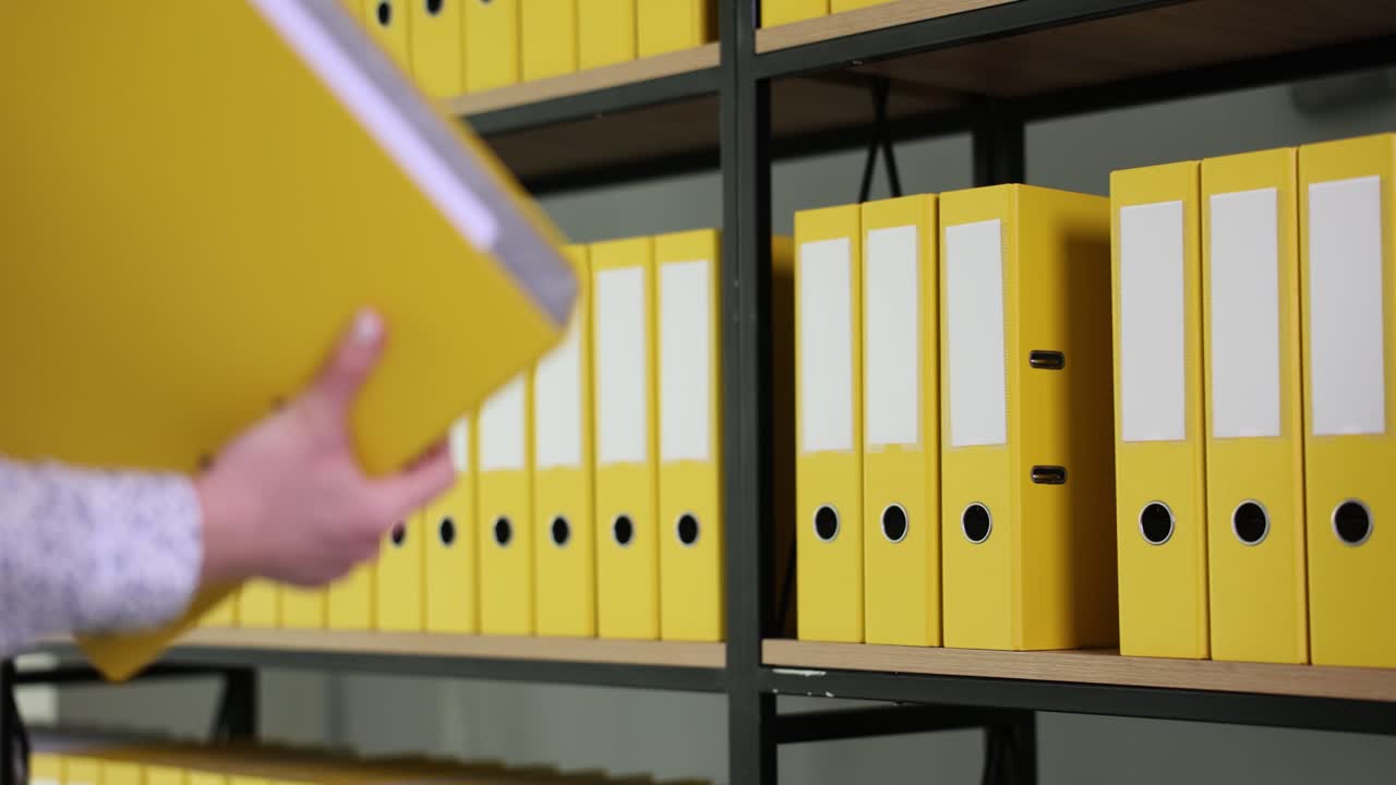 Person taking a yellow binder from an office shelf