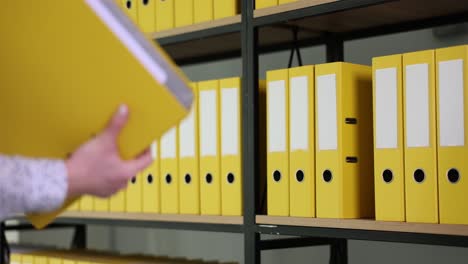 person taking a yellow binder from an office shelf