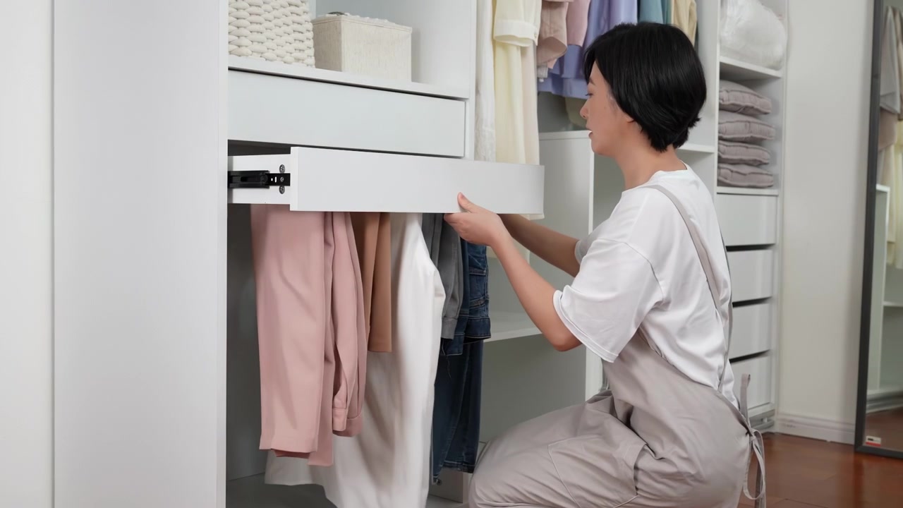 Casalinga con il grembiule che organizza e ripone con cura i vestiti nell'armadio, piegando e sistemando i capi per una conservazione pulita ed efficiente, enfatizzando un ambiente domestico ordinato e organizzato