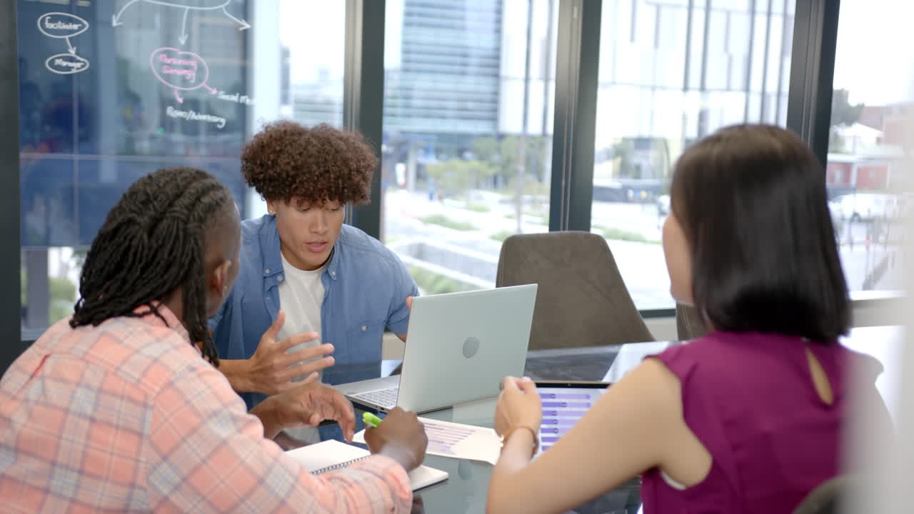 Discussing project ideas, diverse team collaborating in modern office with laptop