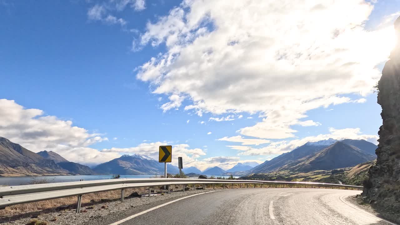 A breathtaking drive through Queenstown's mountainous landscape, capturing serene lake views under a bright, clear sky