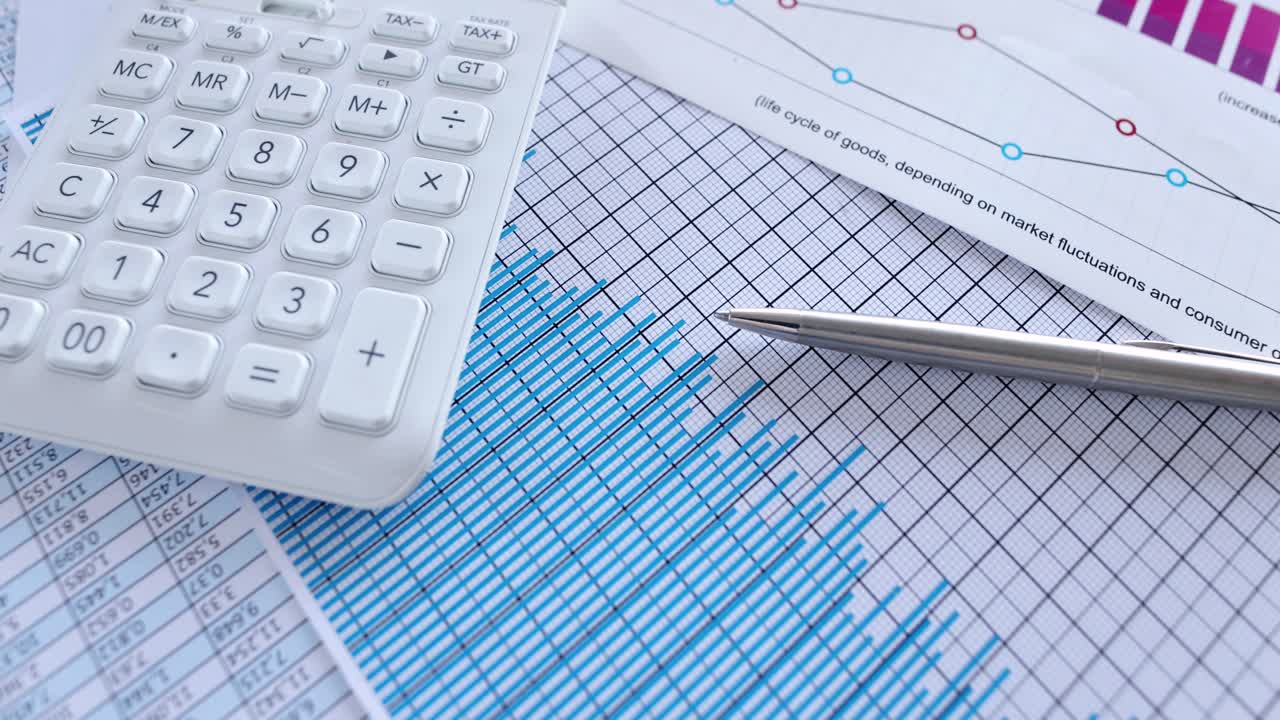 Caneta esferográfica e calculadora sobre documentos com gráficos, close-up, vídeo 4k em câmera lenta