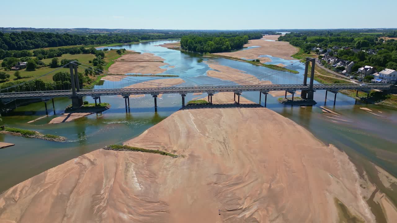 Drone pullback shot showing Varades suspension bridge over low Loire River with visible sandbanks and surrounding vegetation - Loireauxence in France
