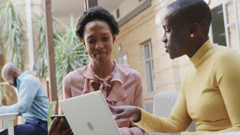 two happy african american businesswomen talking, laughing and using laptop outdoors, in slow motion
