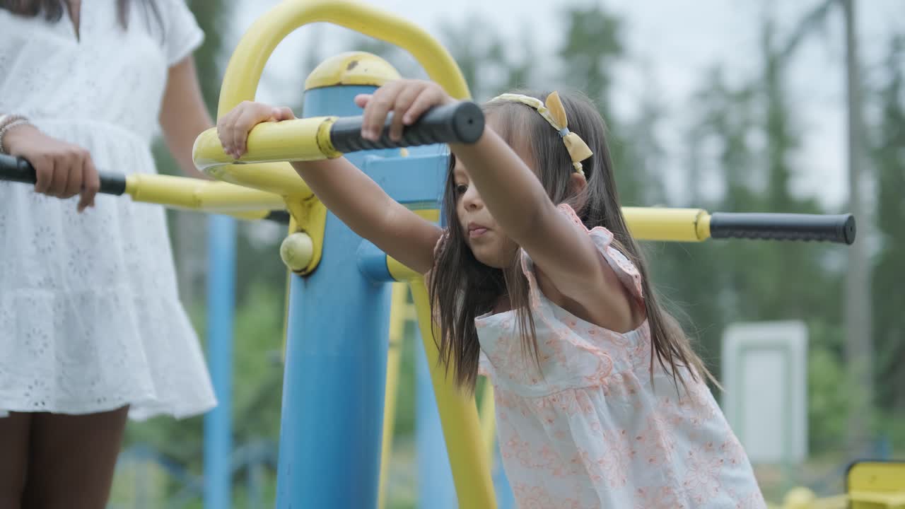 임신 한 어머니 와 어린 딸 은 나무 와 초록색 으로 둘러싸인 공원 의 놀이터 에서 함께 놀이 를 즐긴다