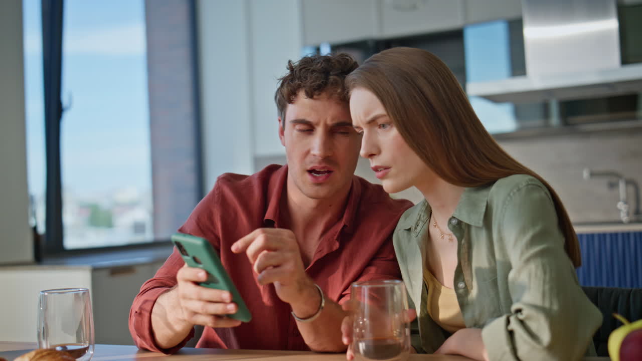 Puzzled couple looking cellphone at home breakfast closeup. Disappointed spouses