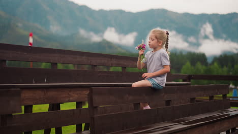 little girl enjoys wildflowers aroma sitting on wooden bench