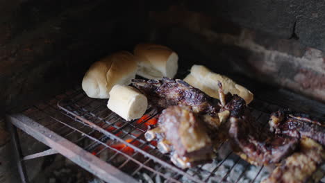 freshly baked bread rolls and juicy beef ribs grilling together on a traditional argentine wood-fired parrilla, glowing embers beneath, rustic brick barbecue, smoky aroma, authentic asado atmosphere