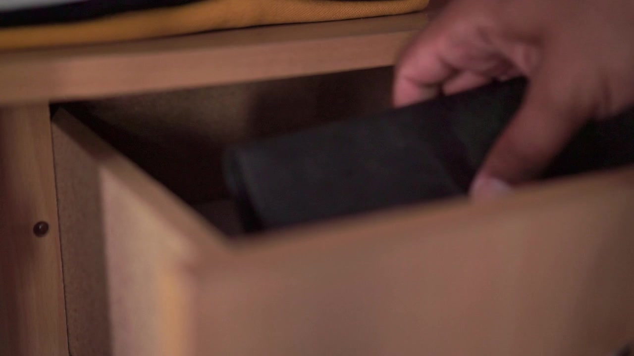 Mano che apre delicatamente il cassetto di un mobile in legno e prende un libro nero. Dettaglio di arredamento interno, gestione dello spazio domestico e routine domestica quotidiana