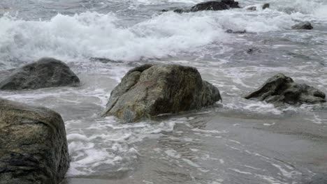 close up on coastal waters with ocean foaming waves crashing around submerged rocks half above surface