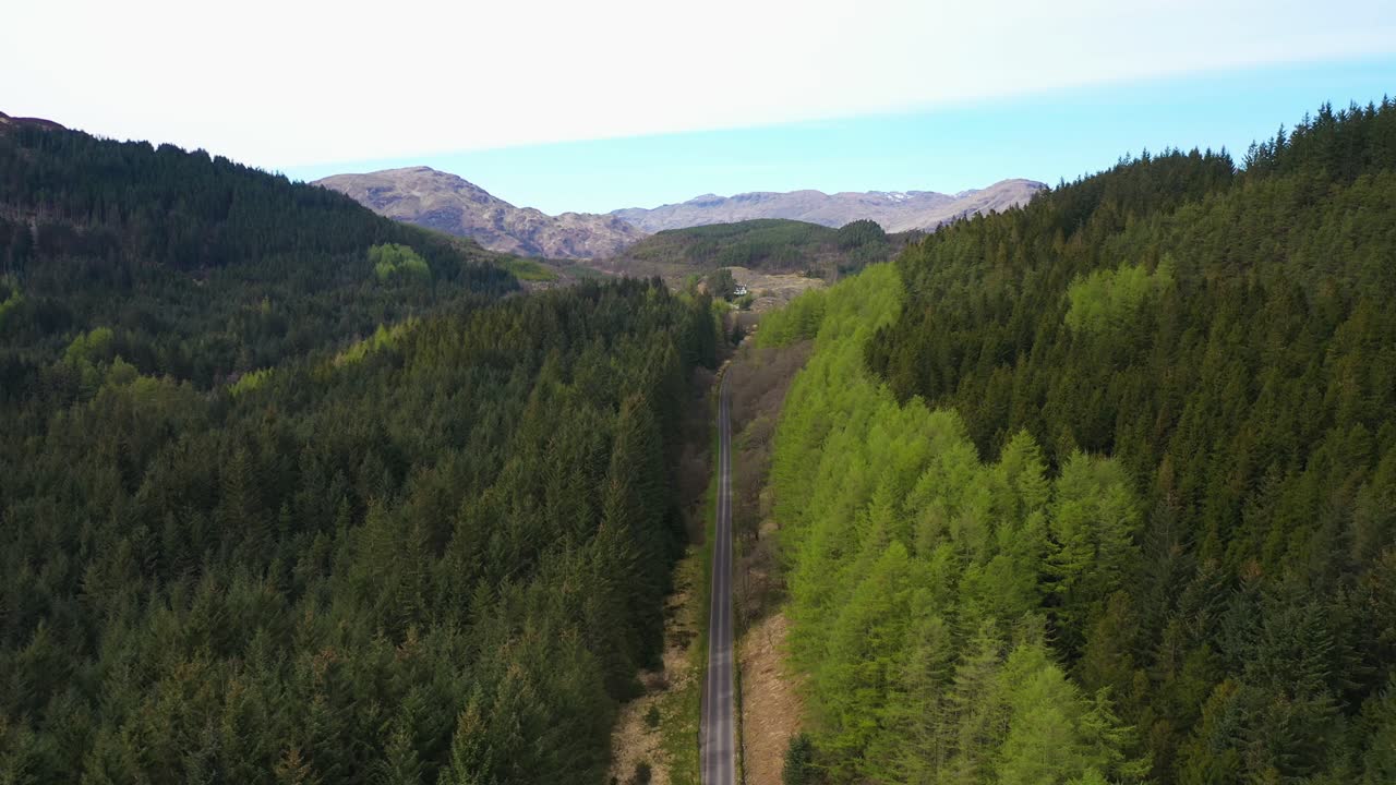 Aerial view of a road passing through a dense forest valley with mountains in the background
