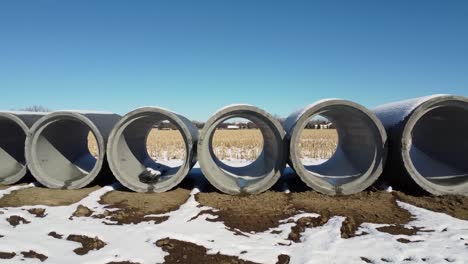 Drone-Shot-Looking-Though-Concrete-Pipes-At-Snow-Covered-Wheat-Field