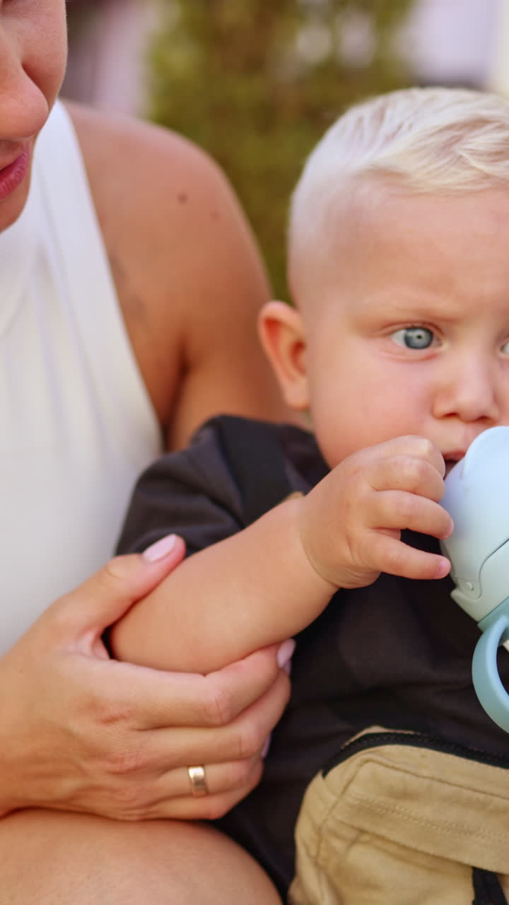 Bambino di un anno beve acqua da una bottiglia per strada. Il bambino beve acqua durante una passeggiata. Benefici dell'acqua per i bambini. Una bottiglia con cannuccia per bambini