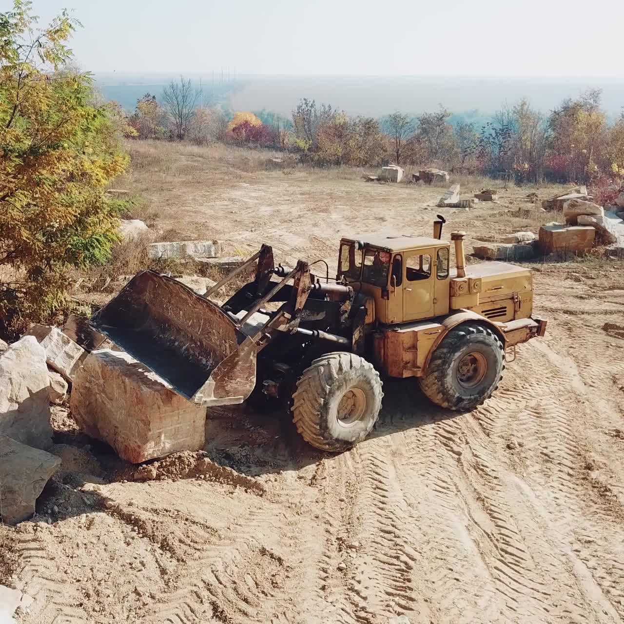 professional yellow bulldozer with a bucket is working in the quarry with stones on the background of sand. Close-up