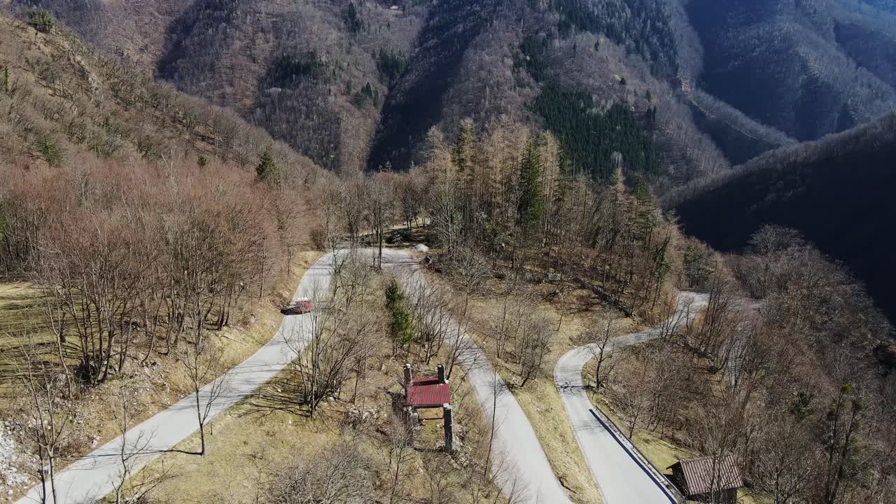 Drone captures red car navigating winding scenic mountain road through Slovenia