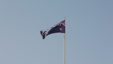 an australian national flag on a flag pole flaps in the wind on a little breeze day in australia