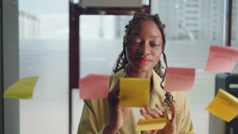 african american business woman write tasks creative ideas on sticky notes on glass board female corporate leader planning project on post it sticky notes organize work on stickers