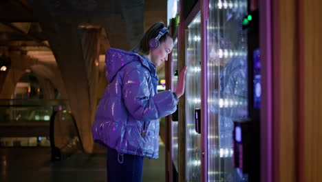 woman buying snacks vending machine at subway late evening. girl make purchase.