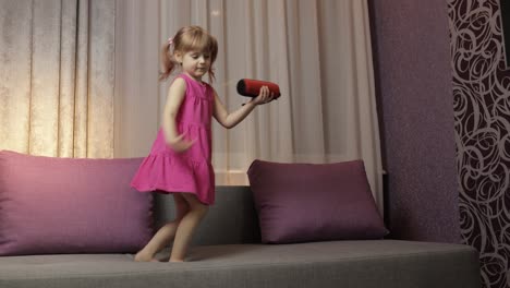 child girl with wireless speaker enjoying listen music. dancing on sofa at home