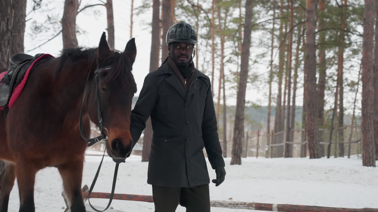frío paseo al aire libre junto a un compañero equino, individuo acompañado por un caballo a través de un paisaje invernal, altos pinos y un pueblo distante enmarcan a un hombre caminando con un caballo en un entorno nevado