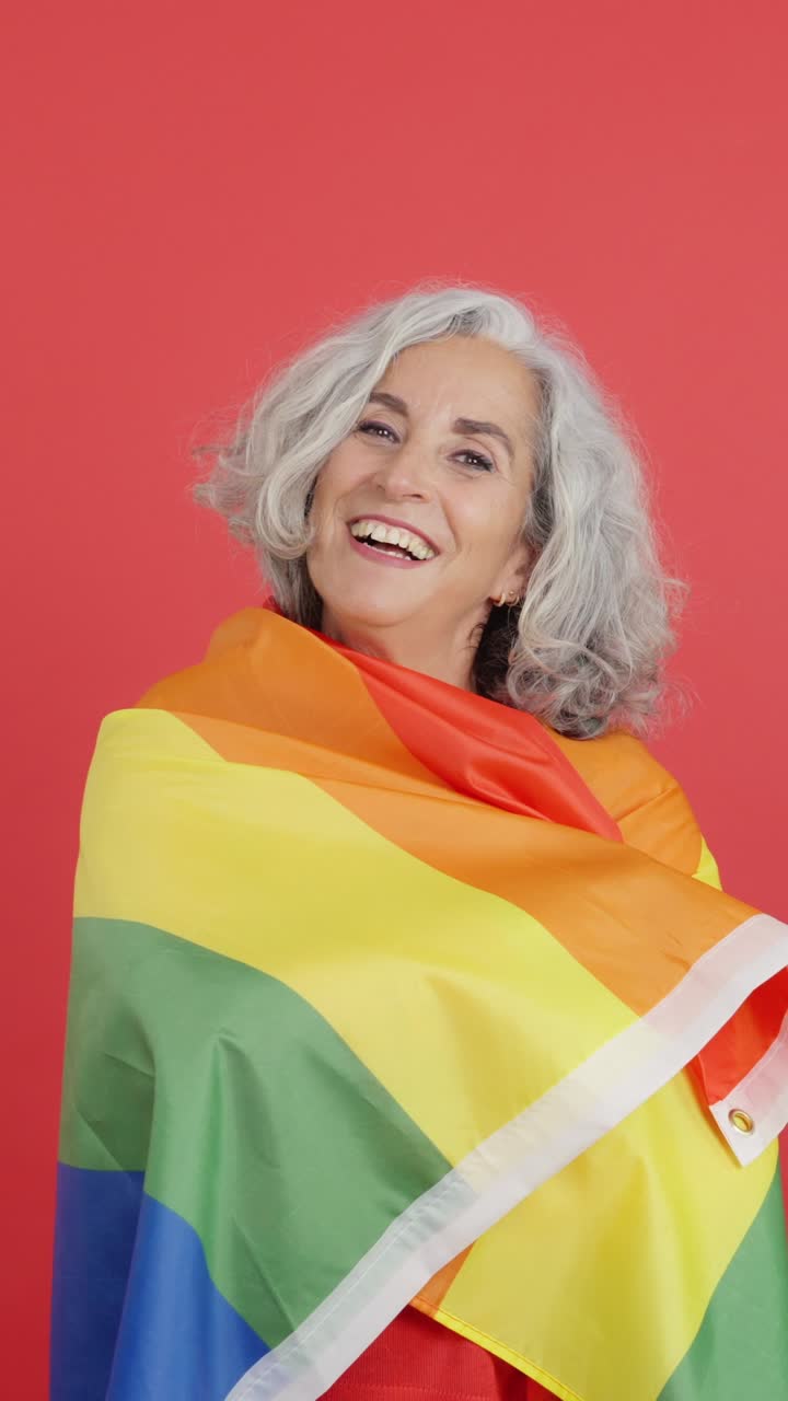 Smiling senior woman wrapped in rainbow flag