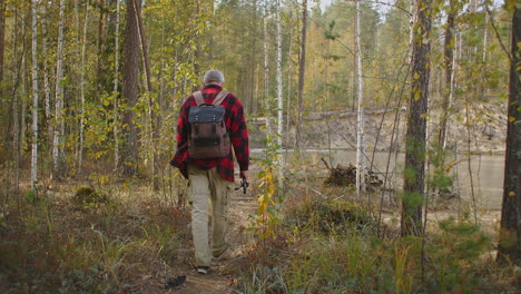 Fischer-Mit-Rute-Und-Rucksack-Geht-Am-Herbsttag-In-Vergilbten-Bäumen-Und-Trockenem-Gras-Durch-Den-Wald-Zum-Fluss