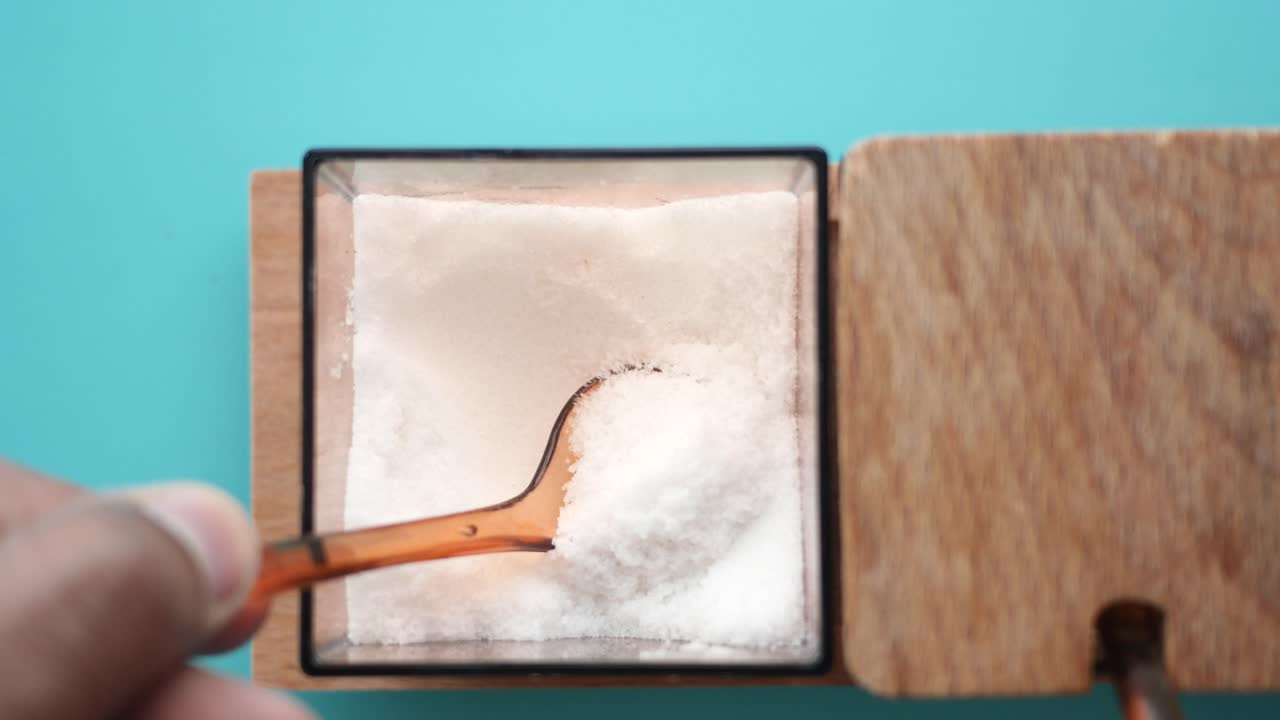 primer plano de una mano recogiendo sal de un recipiente de madera
