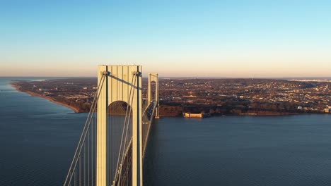 aerial tracking shot passing the verrazzano-narrows bridge with staten island in the background, fall sunset in ny, usa