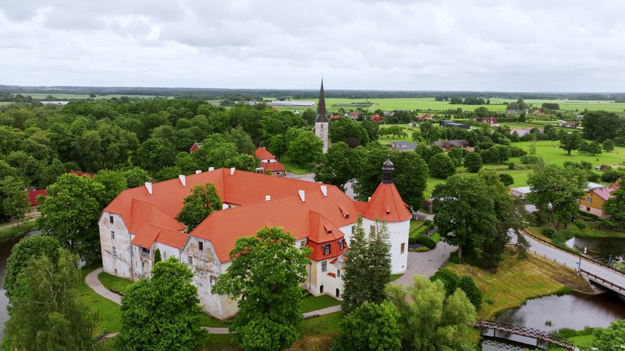 Drone si avvicina al Castello di Jaunpils attraverso i campi verdeggianti della Lettonia sotto cieli grigi