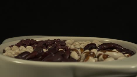 low angle revolving bowl of dry beans on black background, close-up