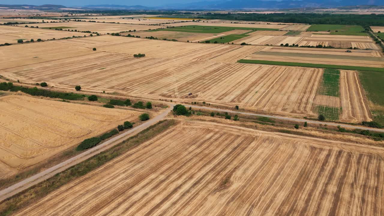 Smooth aerial push shot over expansive orange and green agricultural fields divided by scattered trees, with hazy blue hills lining the horizon