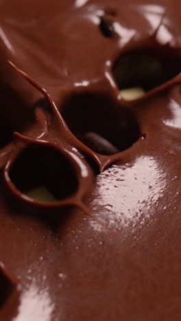 vertical video close up overhead shot of pieces of chocolate being dropped into melted chocolate sauce