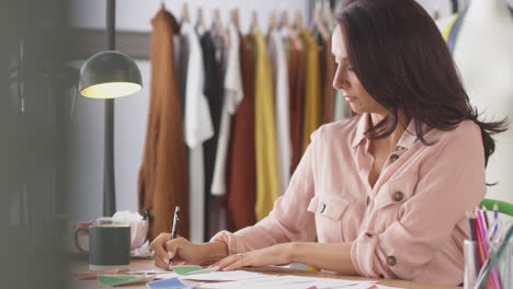 diseñadora de moda en el escritorio en el estudio dibujando diseños y eligiendo muestras de colores y telas