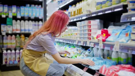 A-girl-with-bright-red-hair-in-an-apron-distributes-goods-at-the-dairy-products-counter-in-a-supermarket